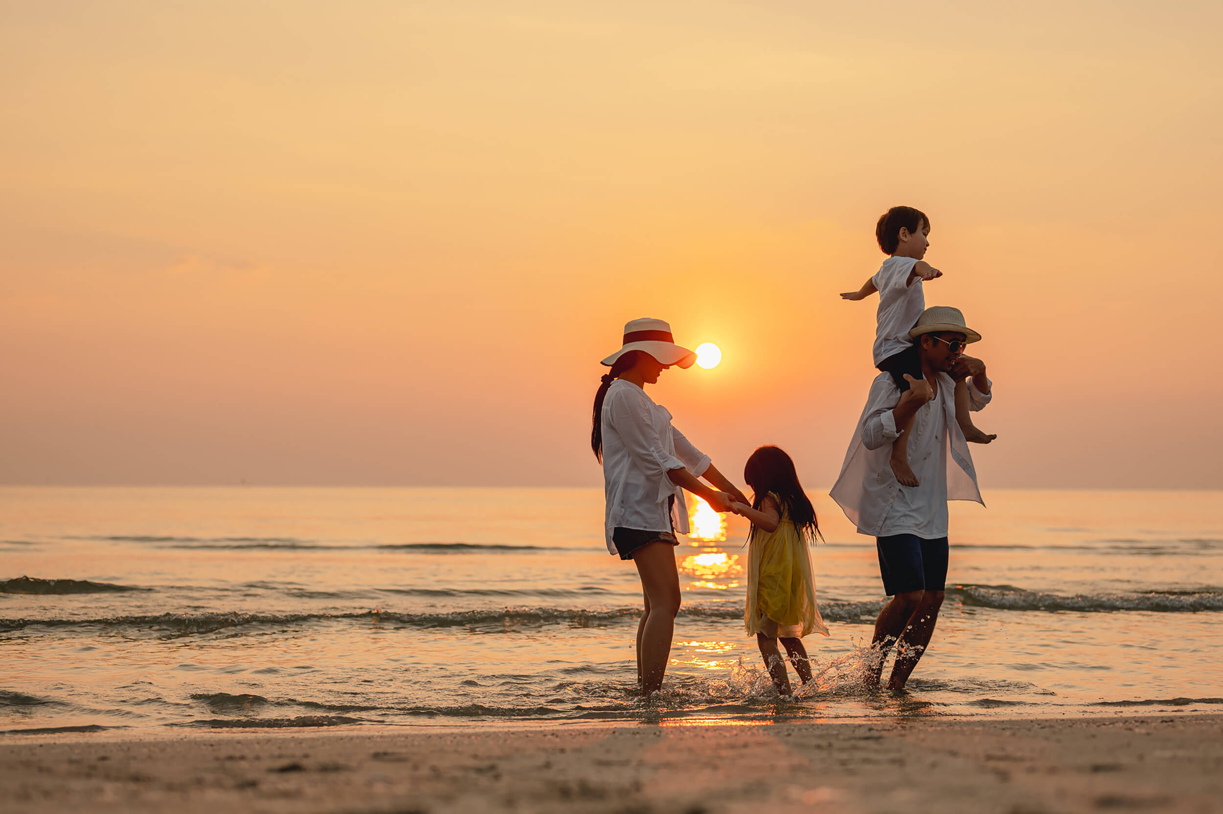 A family plays along the shallow water on the beach at sunset.