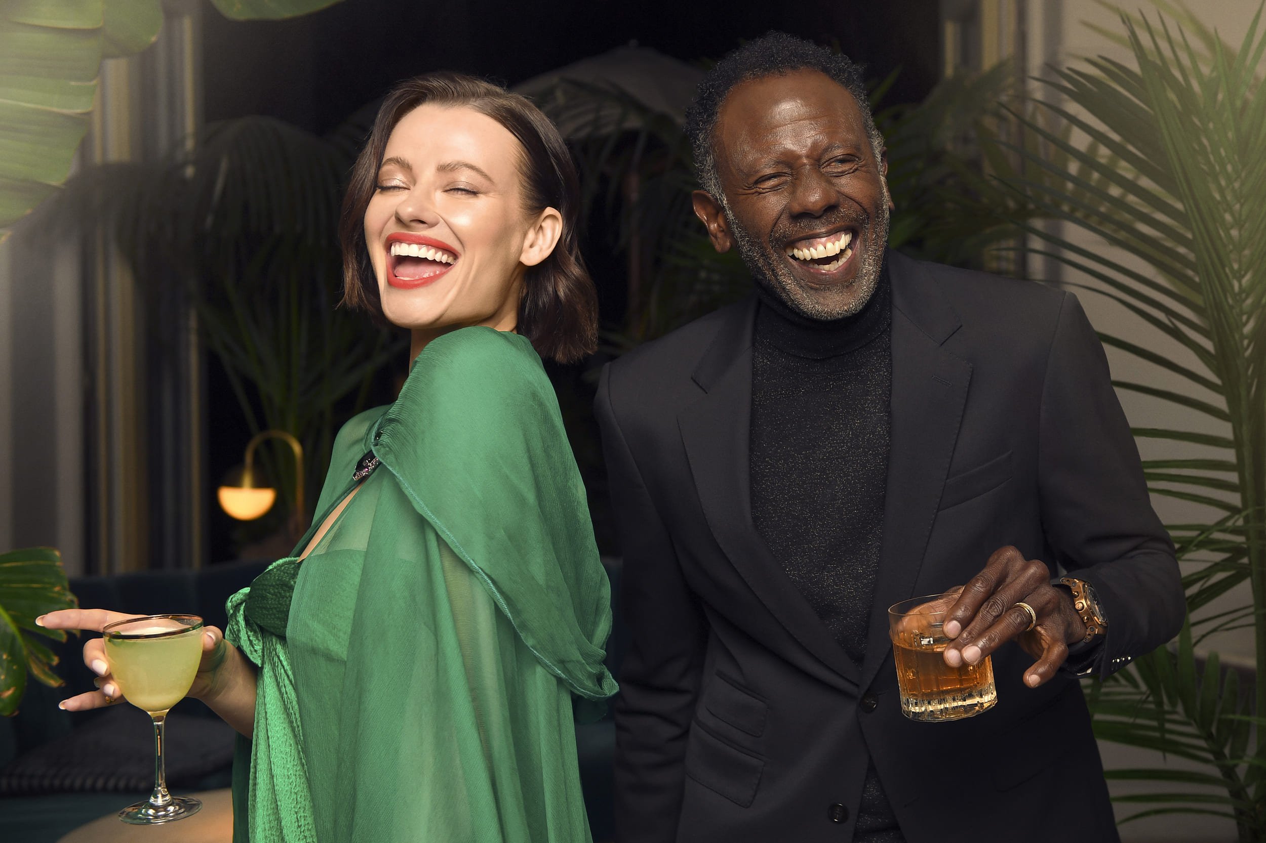 A man and a woman laughing with cocktails in hand.