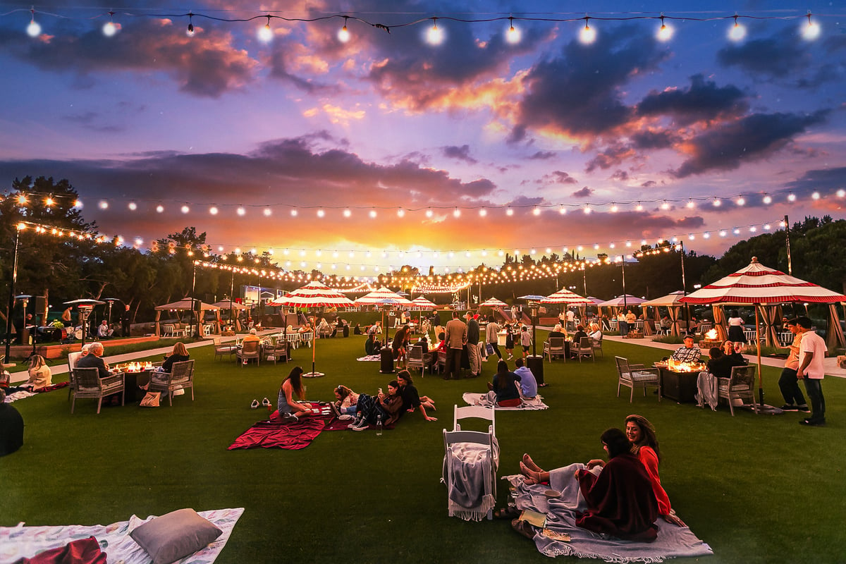 A gathering of people sitting around a green lawn at sunset.