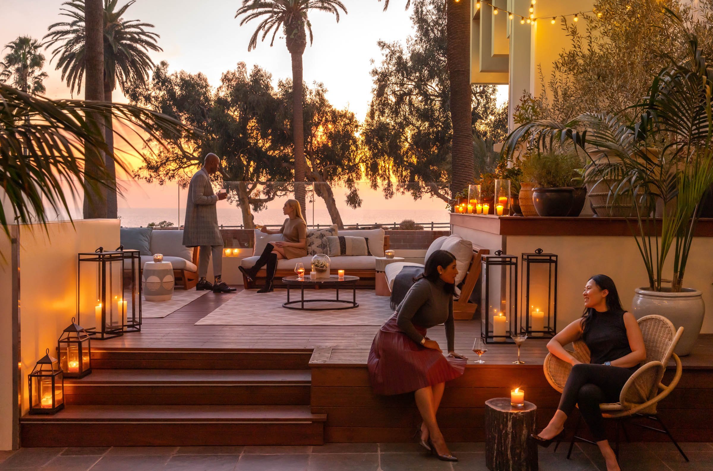 People drinking wine by candlelight on a beachside terrace at sunset.