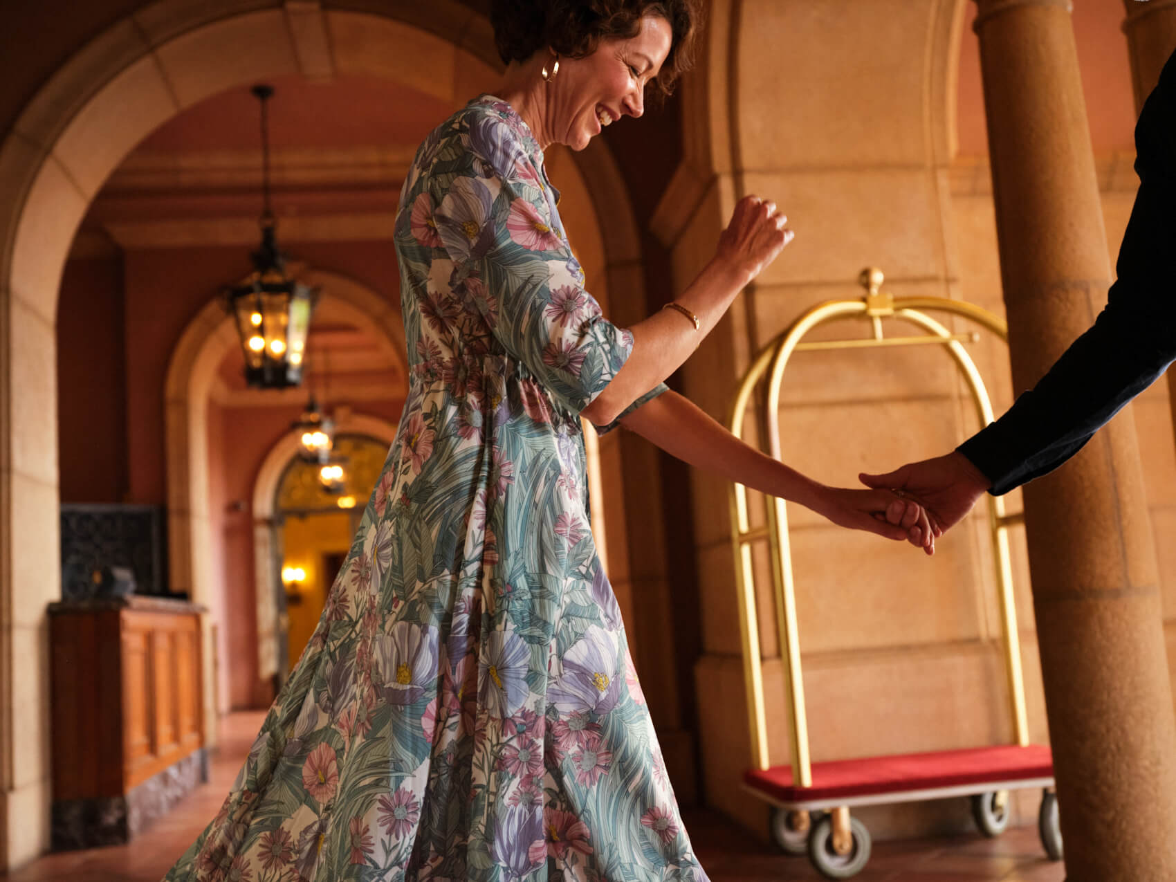 A woman wearing a flowing dress is lead to a hotel lobby.