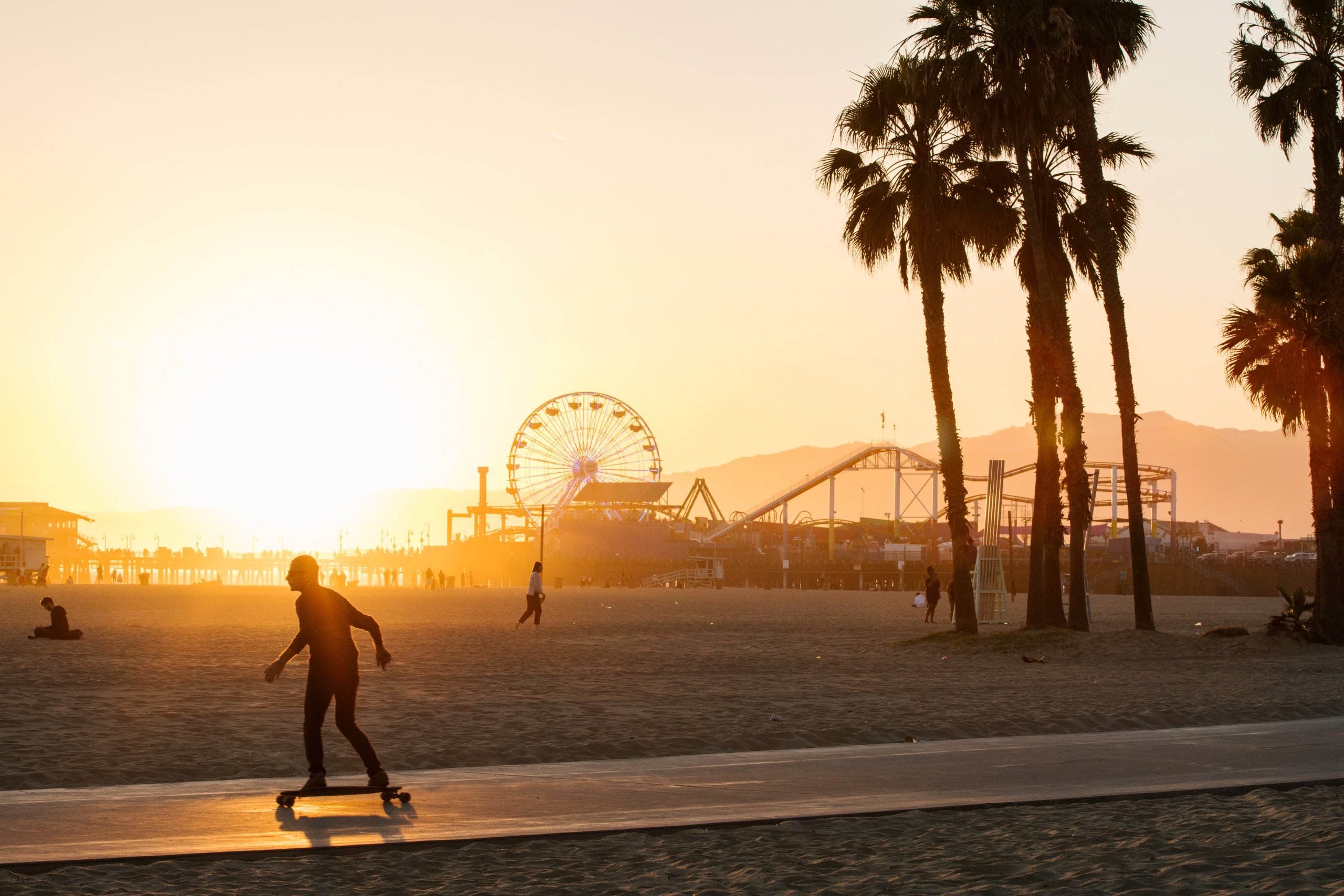 A man long-boarding at Santa Monica Pier at sunset, a theme park in the background.