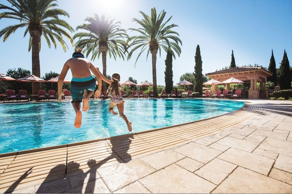 Two children jump into a pool on a sunny day.