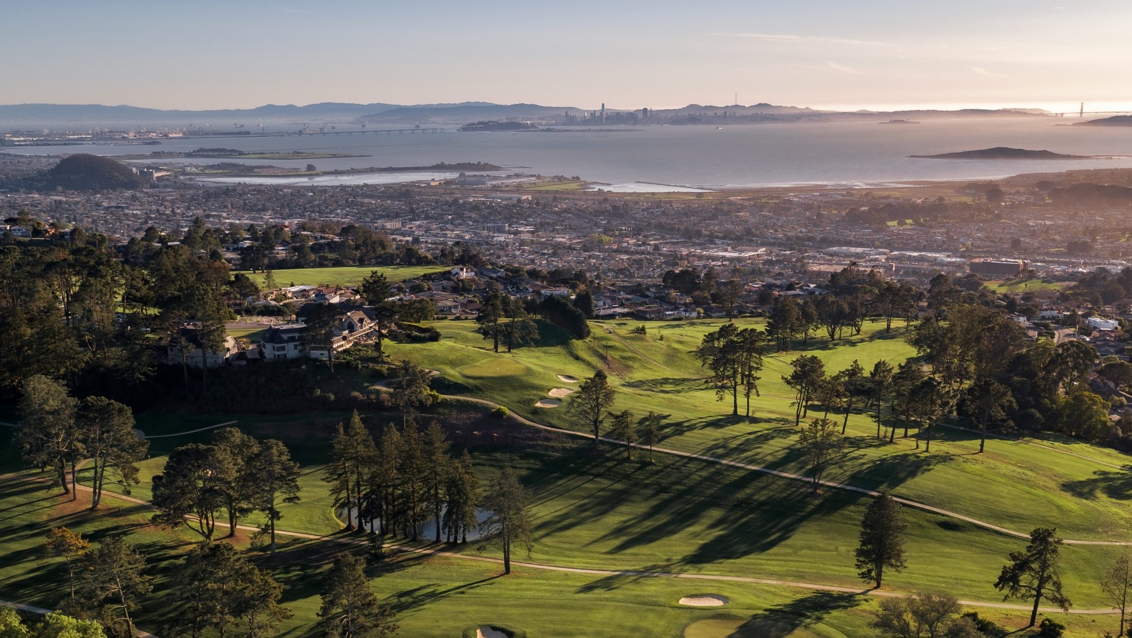 Claremont golf course aerial view at sunset with city and water in the distance.