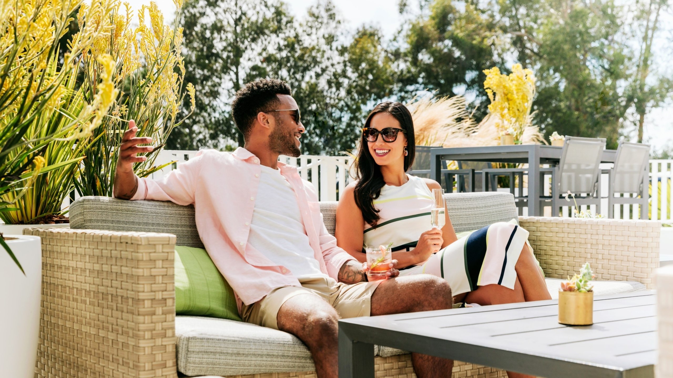 A couple lounges on an outdoor couch with drinks.