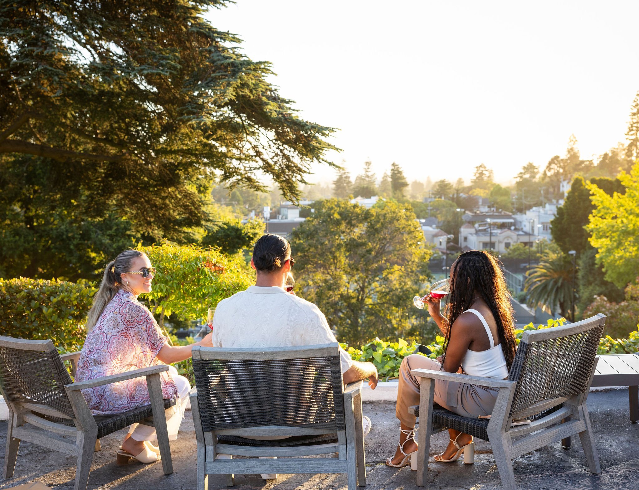 Three people sitting on a patio terrace drinking wine.