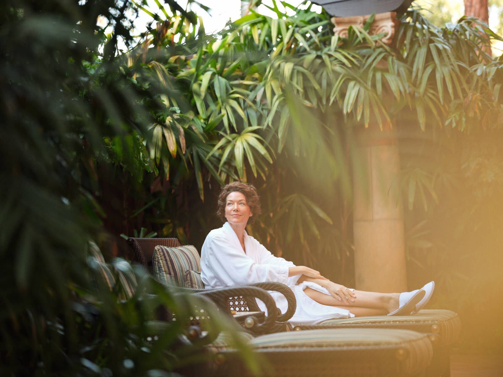 A woman in a white spa robe lounging on a lush outdoor getaway at Fairmont Grand Del Mar.