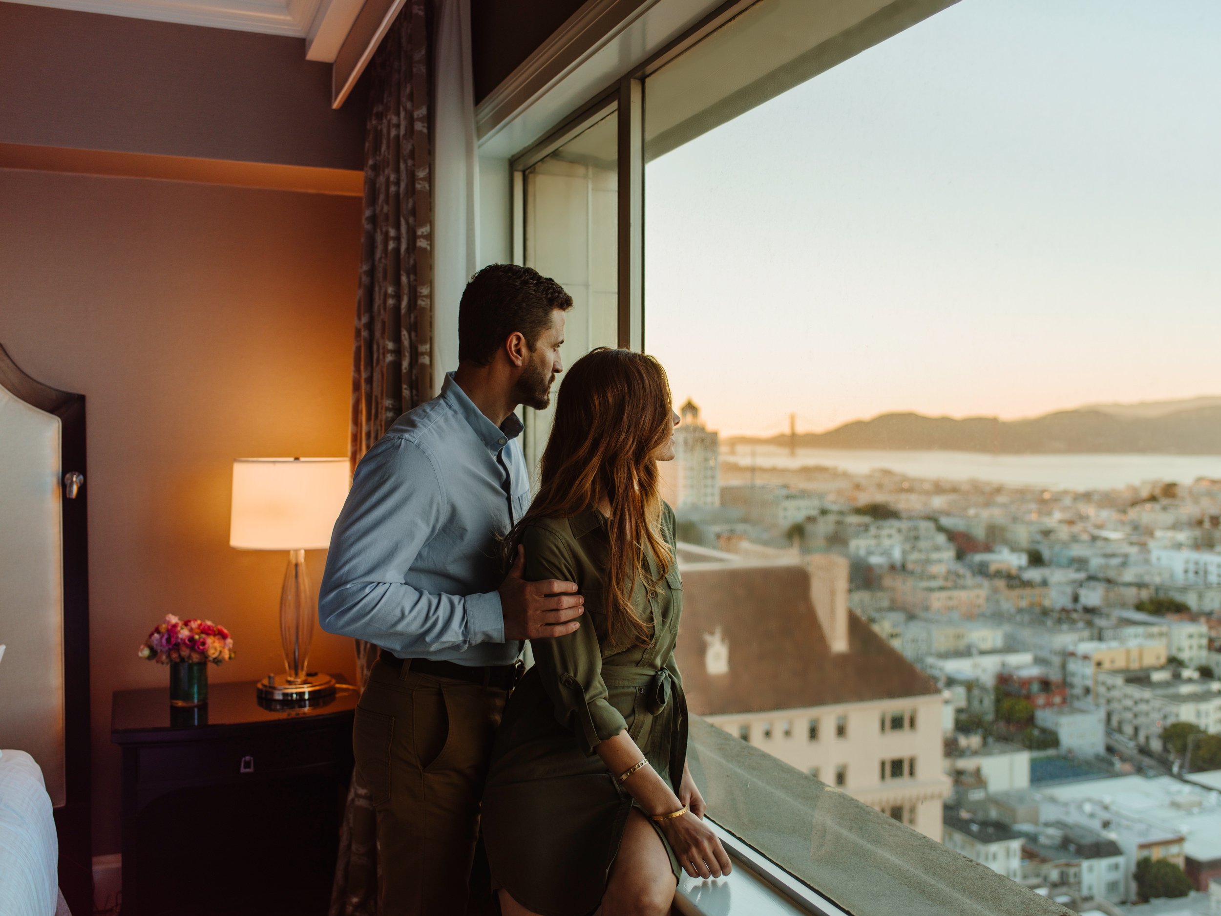 A couple looking out on the city landscape from their hotel room window.