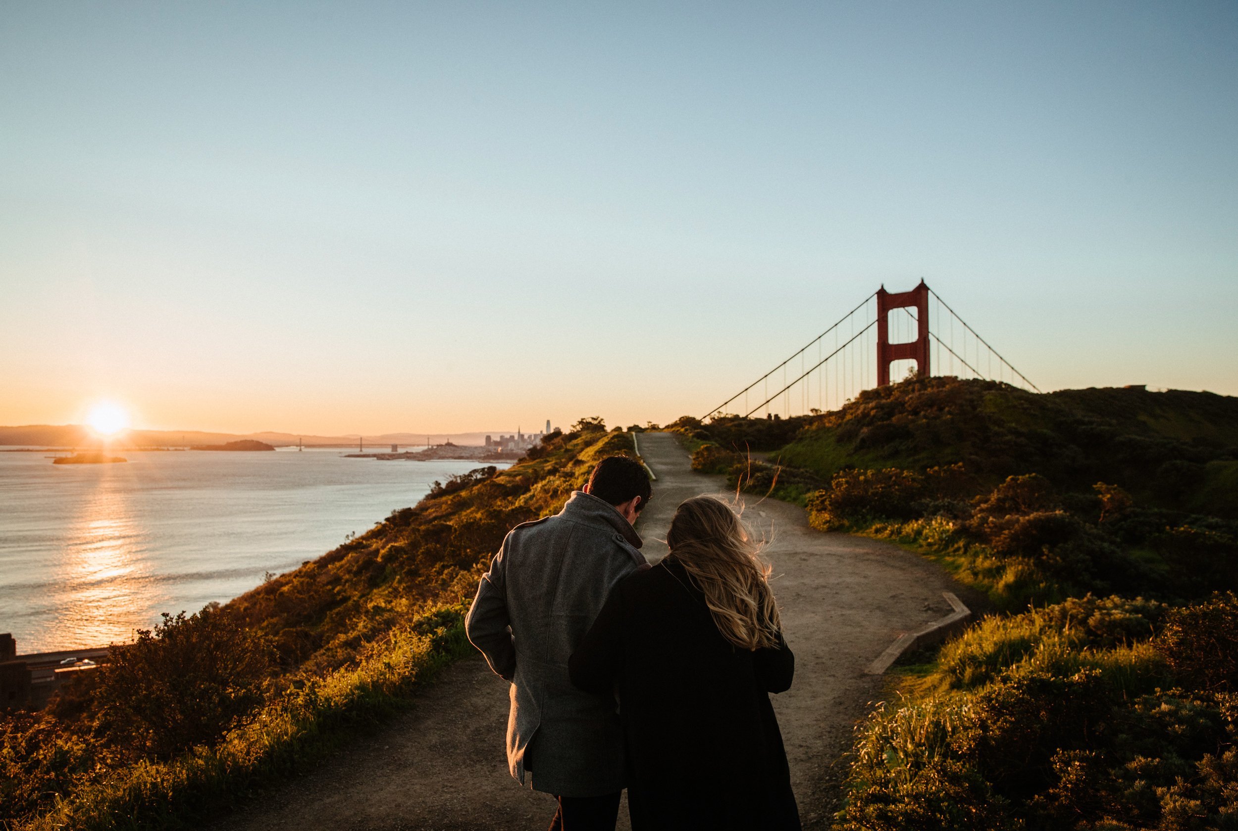 A couple walking on a trail at sunset overlooking the ocean and San Francisco.