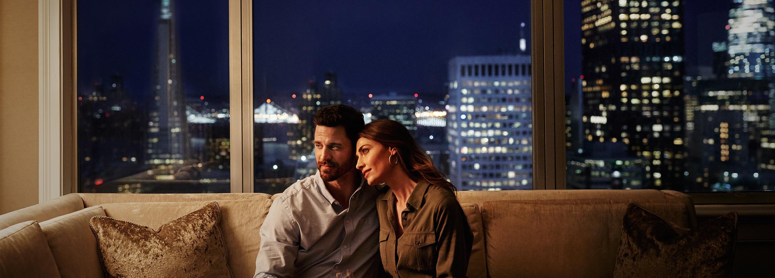 A couple sits together on a couch in a suite overlooking San Francisco.